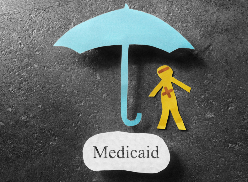 The word 'Medicaid' underneath a paper cutout umbrella and paper cutout person with bandages.
