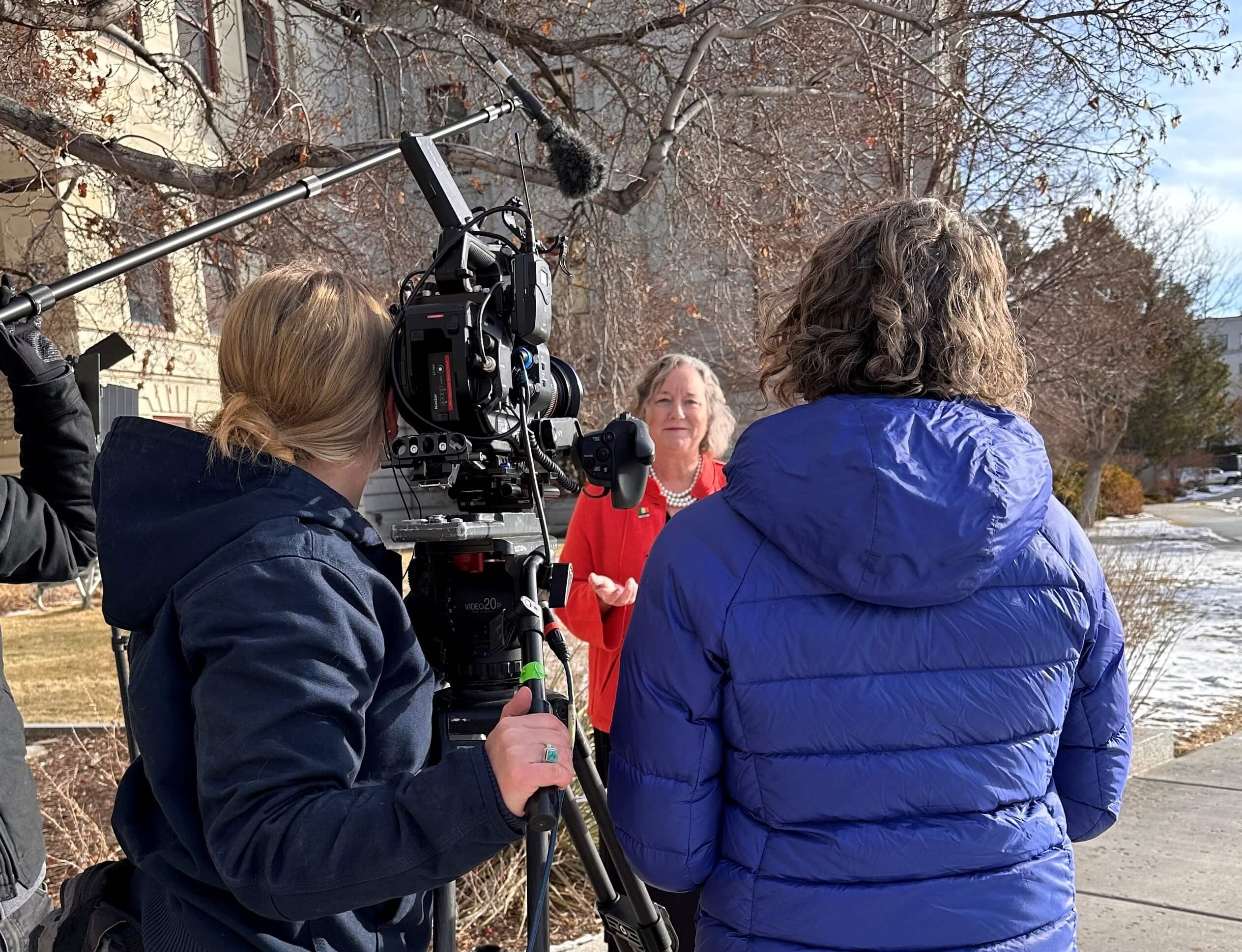 a politician is interviewed by 2 women. One holds a camera, one asks questions.